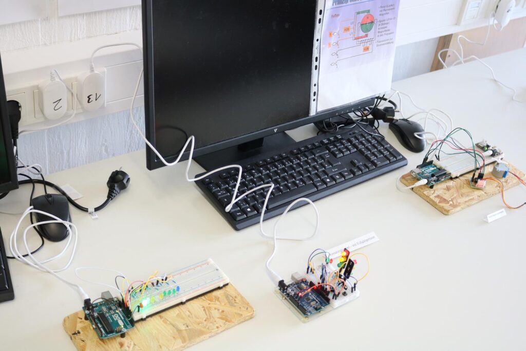 Arbeitsplatz mit Computer und mehreren Mikrocontrollern auf Tischen.