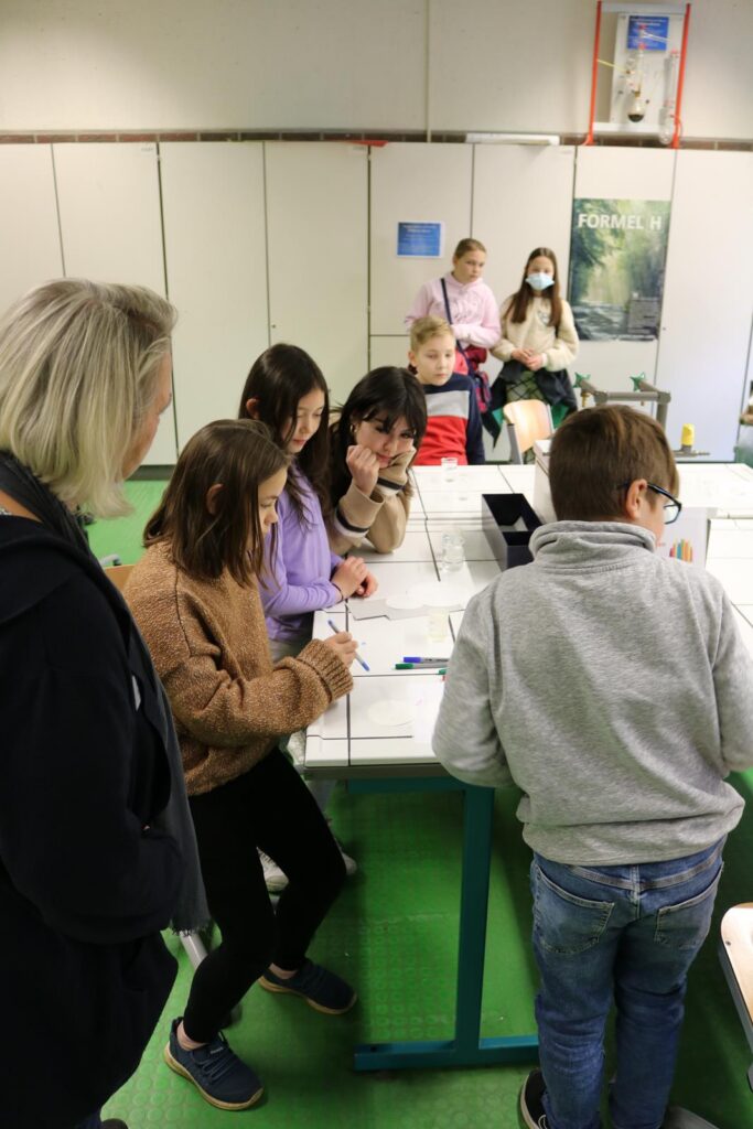 Schülerinnen und Schüler arbeiten an einem Tisch in einem Klassenraum.