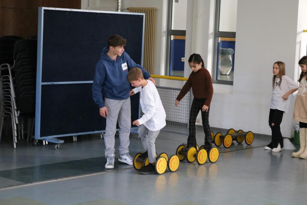 Schüler üben das Balancieren auf einer Reihe von Rollen in einer Turnhalle.