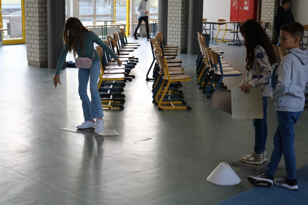 Kinder stehen in einem Flur und üben das Balancieren auf einer Platte.
