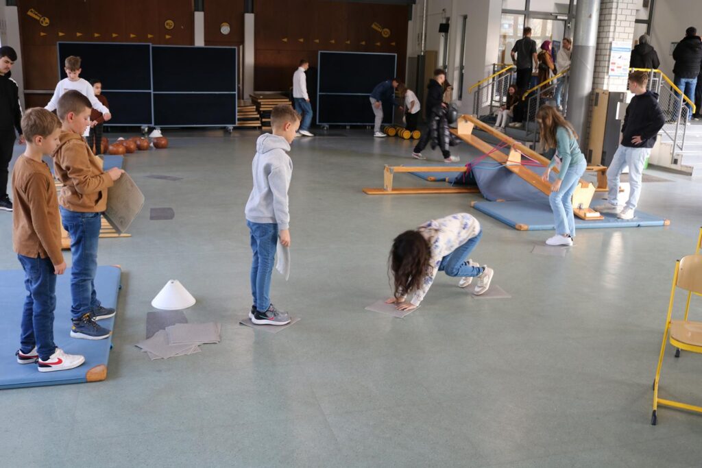 Schüler üben in einer Turnhalle mit verschiedenen Geräten und Matten.