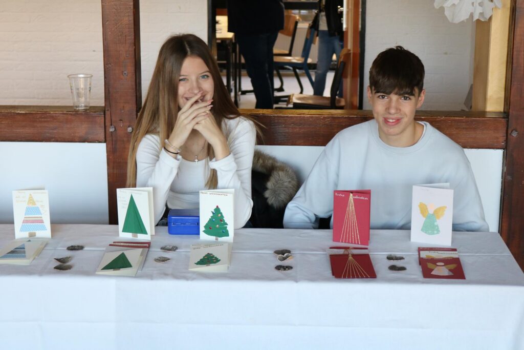 Zwei Schüler stehen an einem Tisch mit Weihnachtskarten und Dekoration.