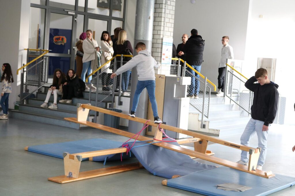 Schüler üben an einem Besenstiel auf einem Turngerät in einer Sporthalle.