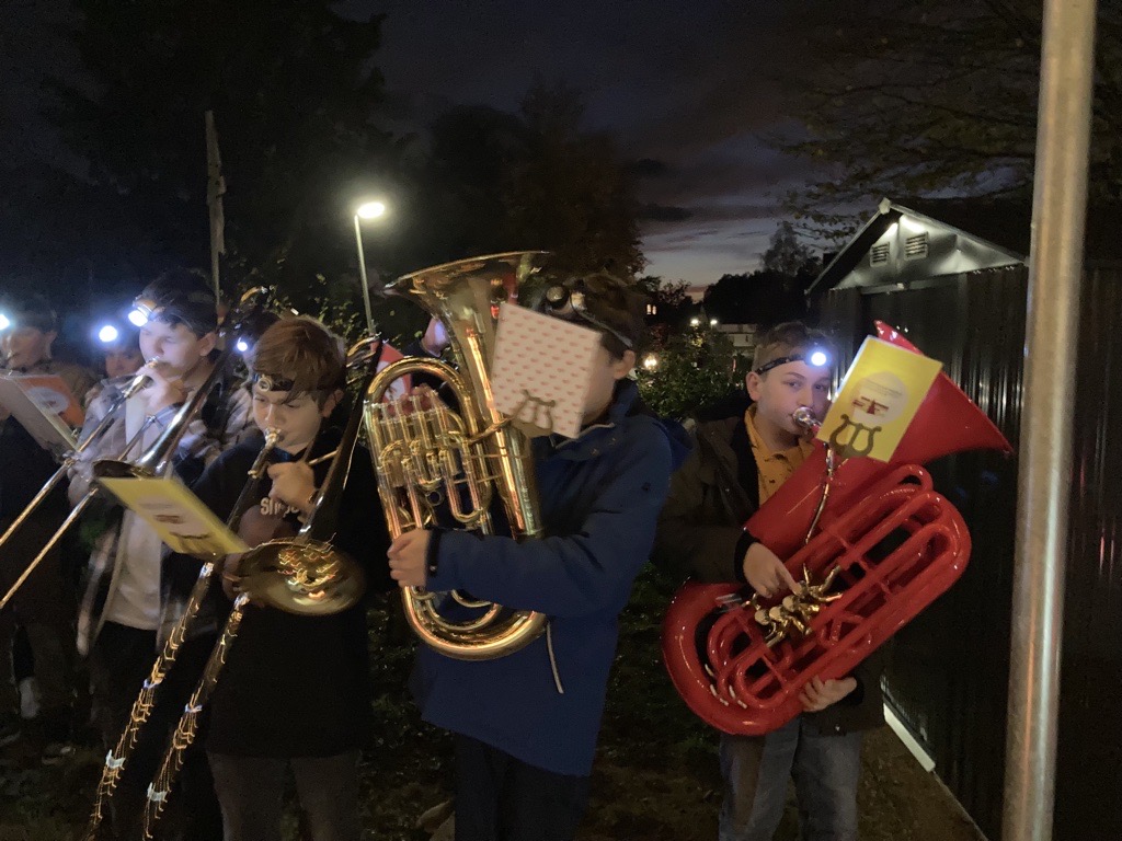Schüler spielen Blasinstrumente bei Nacht, umgeben von Laternenlicht.