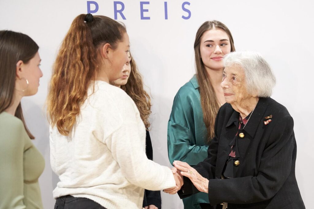 Eine ältere Frau begrüßt eine junge Frau bei einer Preisverleihung.