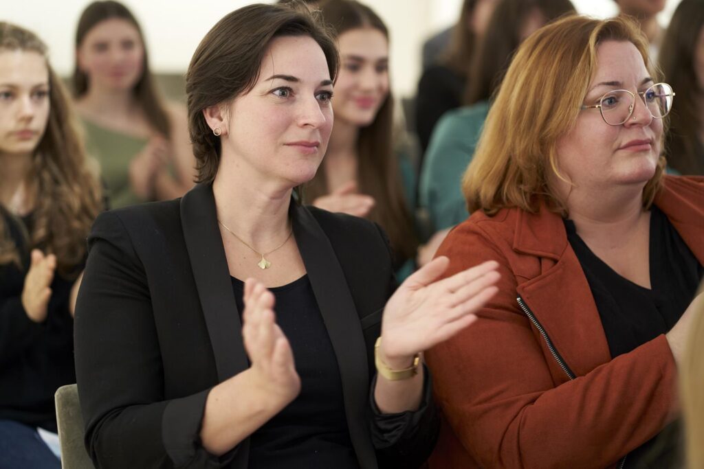 Zwei Frauen im Publikum applaudieren. Im Hintergrund sind weitere Zuhörer sichtbar.
