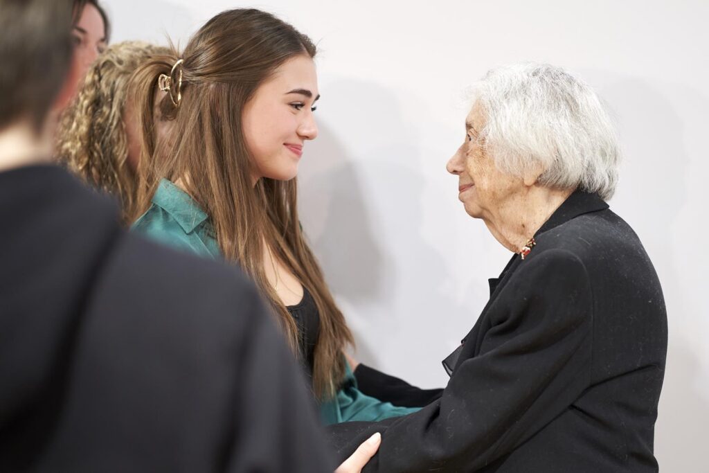 Junge Frau und ältere Dame stehen sich gegenüber und lächeln sich an.