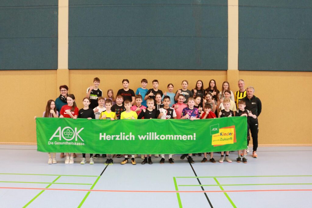 Gruppenfoto von Schülern mit einem Willkommen-Banner in einer Sporthalle.