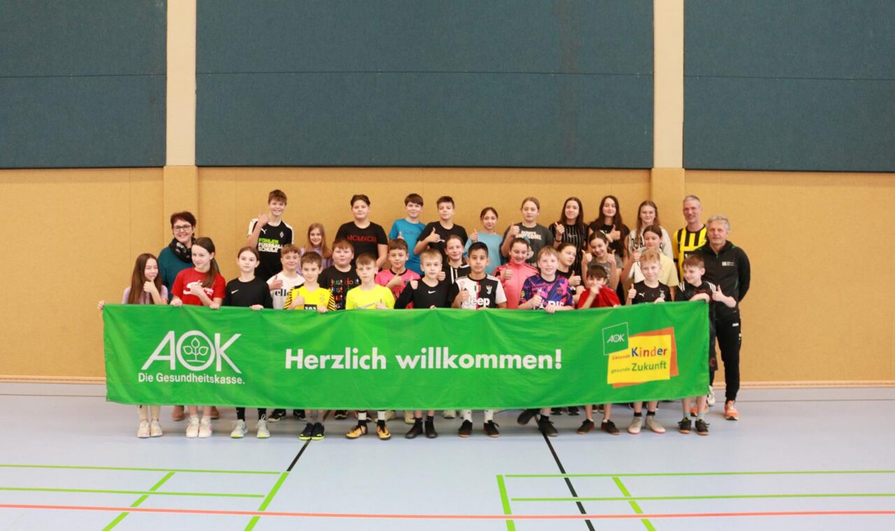 Gruppenfoto von Schülern mit einem Willkommen-Banner in einer Sporthalle.