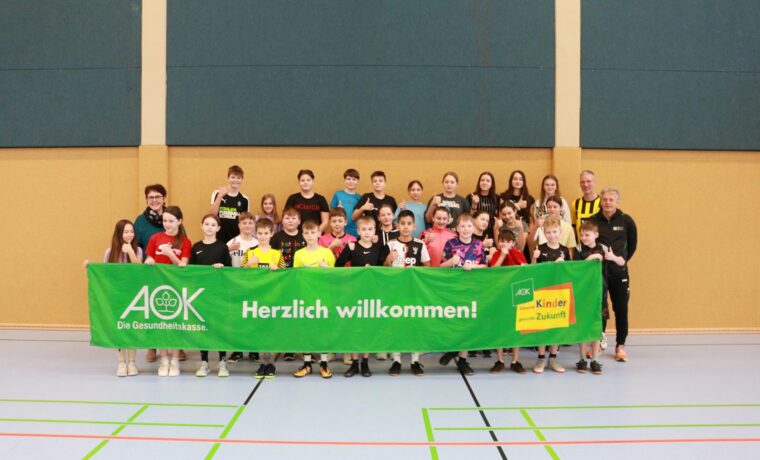 Gruppenfoto von Schülern mit einem Willkommen-Banner in einer Sporthalle.