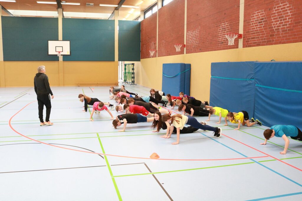 Schülerinnen und Schüler machen Liegestütze in einer Sporthalle.