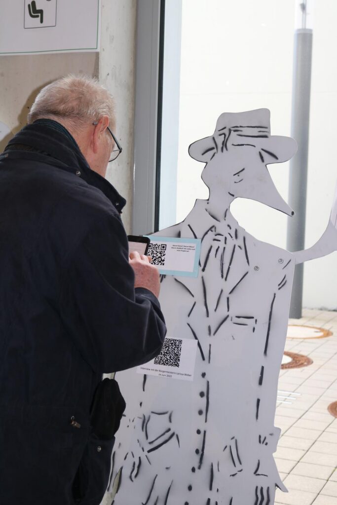 Ein Mann scannt einen QR-Code an einer Pappfigur in einem Flur.
