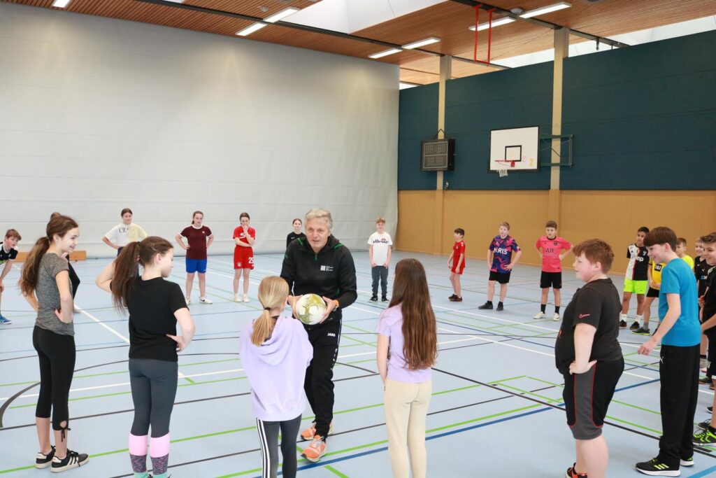 Trainer erklärt den Kindern in einer Sporthalle eine Übung.