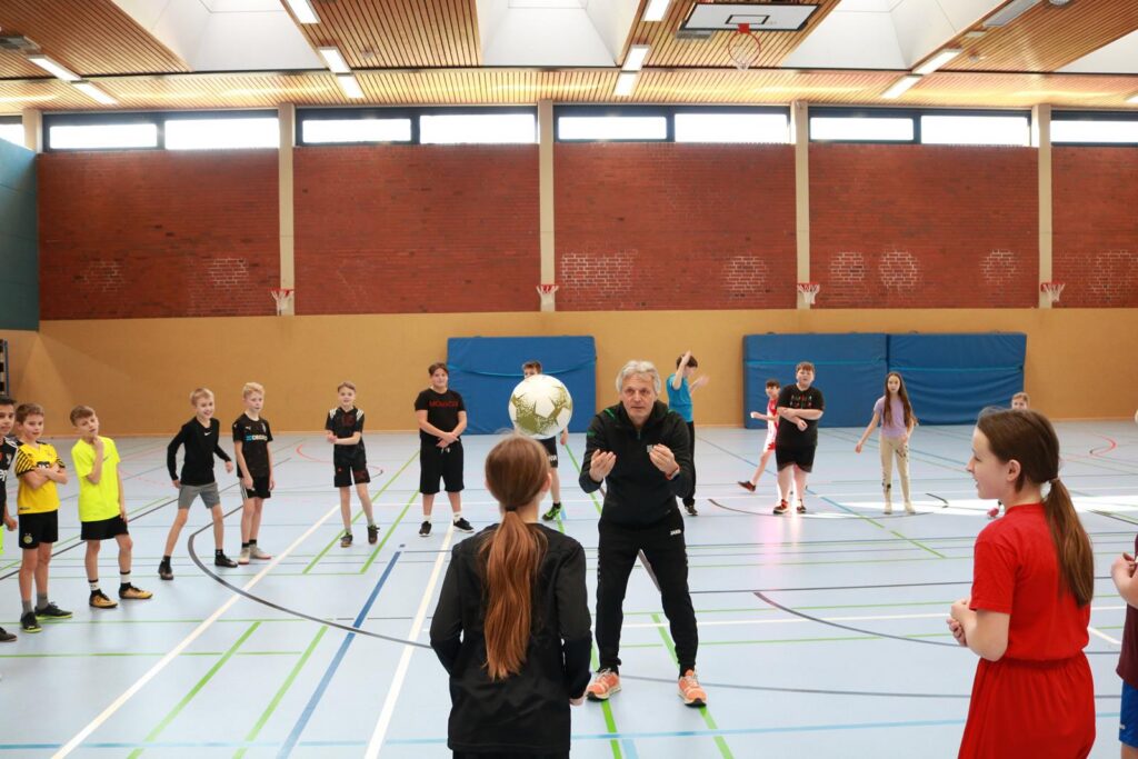 Sportliche Übung in der Halle mit einer Trainerin und Kindern, die Fußball spielen.