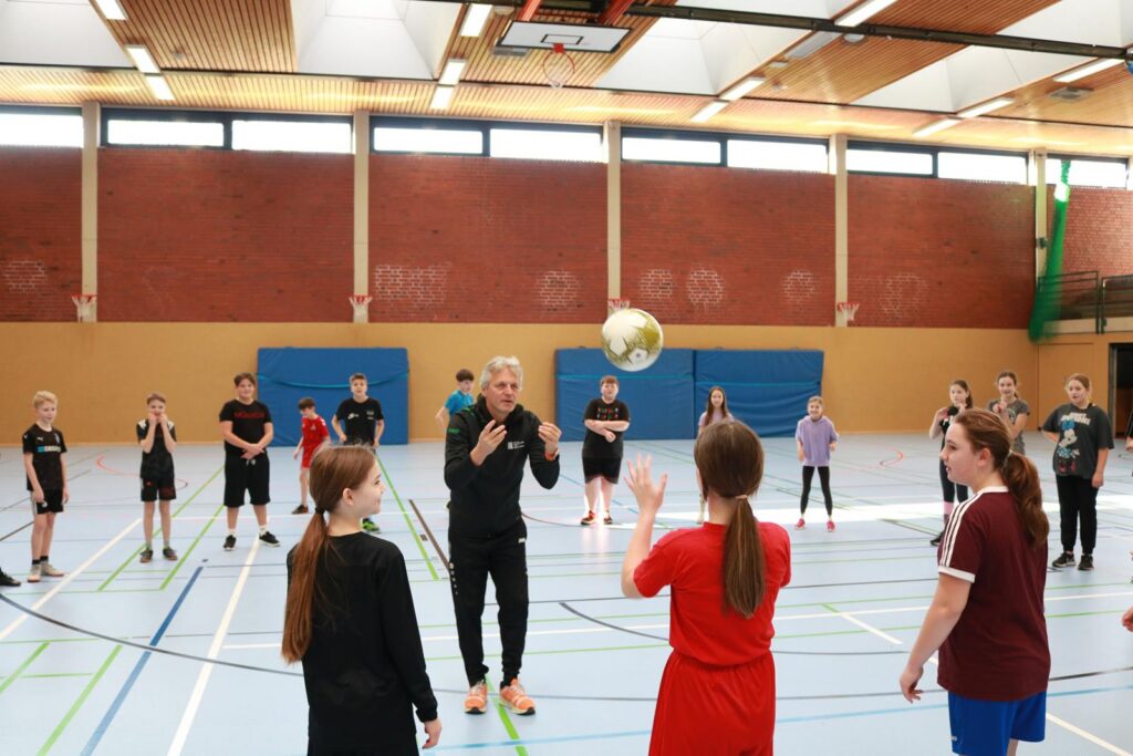 Gruppe von Jugendlichen in einer Sporthalle bei einem Balltraining.