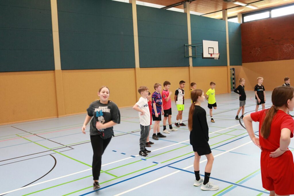 Schülerinnen und Schüler spielen in einer Sporthalle.