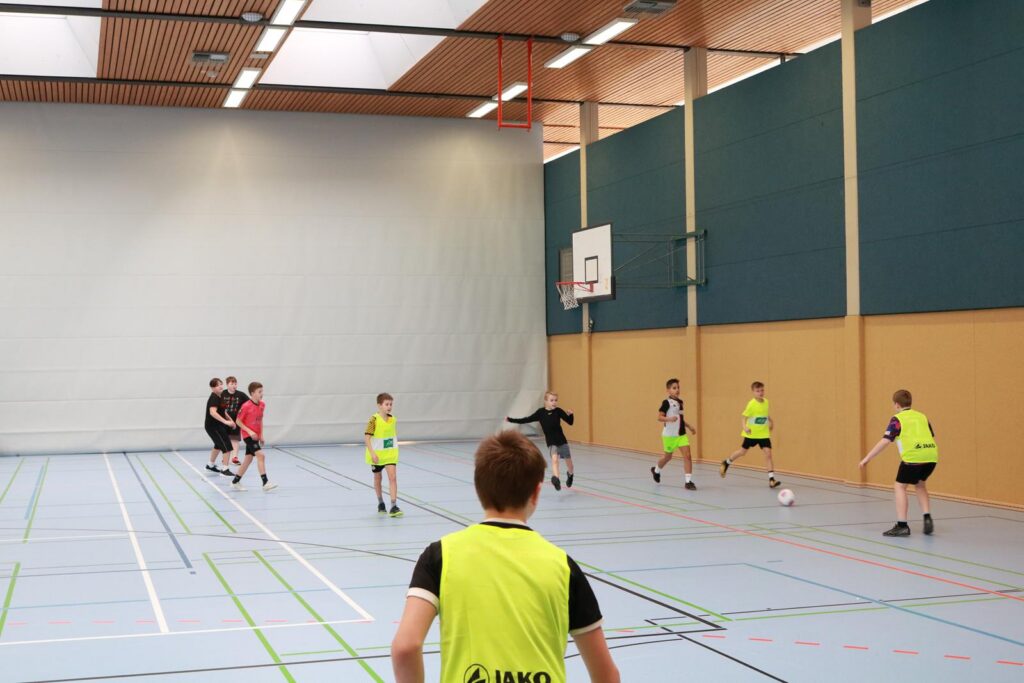 Schüler spielen Fußball in einer Sporthalle.