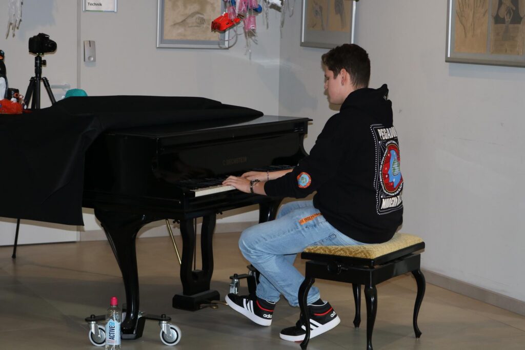 Ein Junge spielt Klavier in einem Raum mit Kunstwerken.