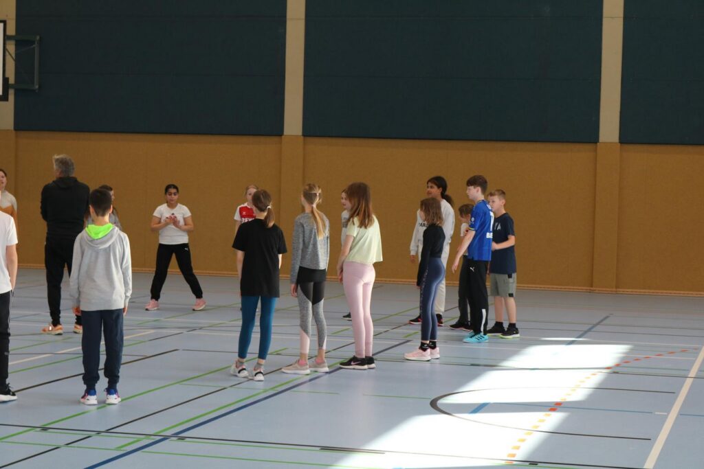 Schülerinnen und Schüler stehen in einer Sporthalle zur Übung bereit.