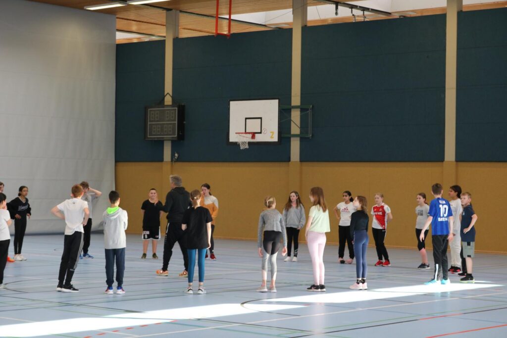 Schülerinnen und Schüler versammeln sich in einer Sporthalle zum Training.