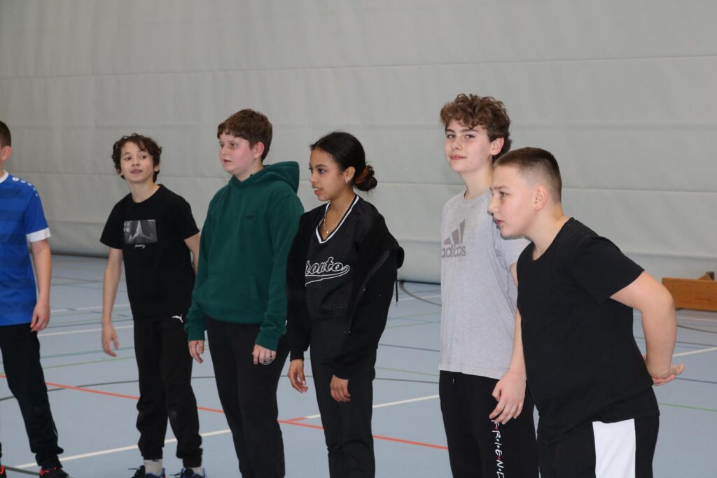 Gruppe von Jugendlichen in Sportkleidung in einer Turnhalle.