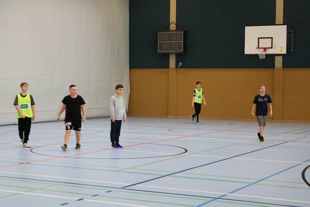 Schüler spielen in einer Sporthalle Basketball.