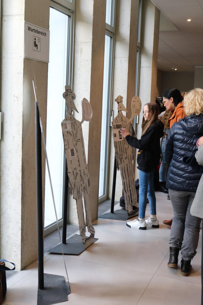 Besucher interagieren mit Pappfiguren in einer modernen Ausstellung.