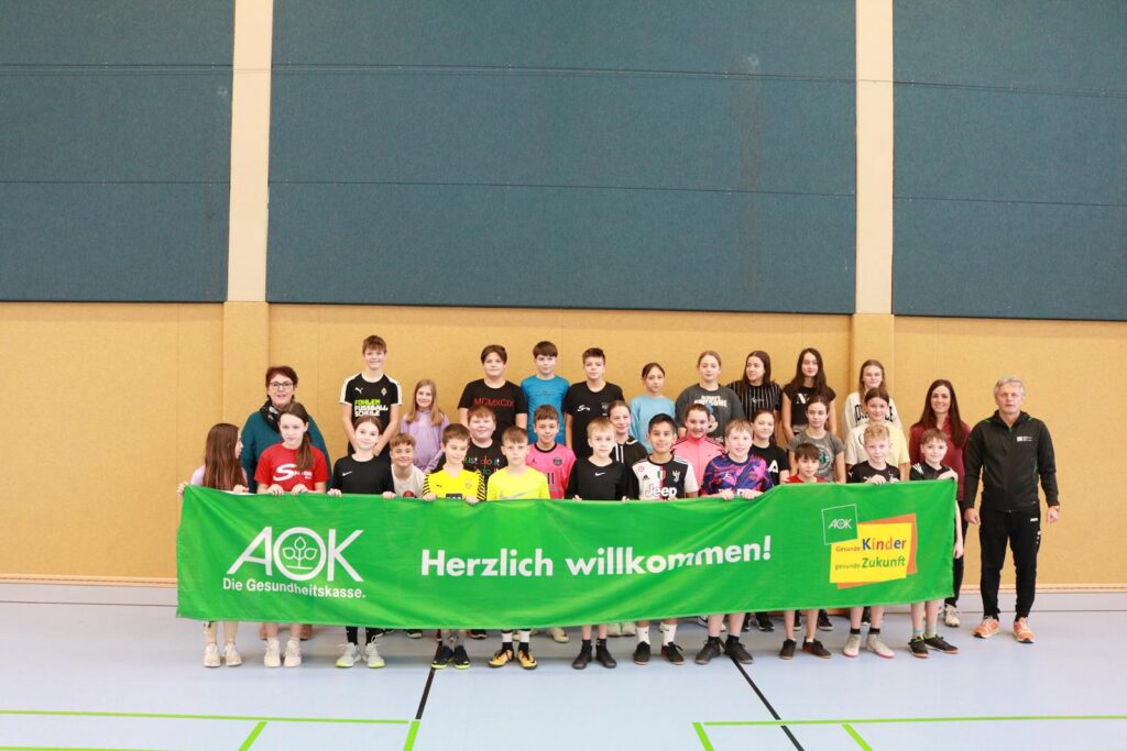 Gruppe von Jugendliche mit einem Banner in einer Sporthalle.