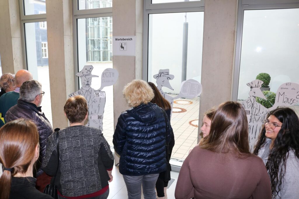 Besucher stehen in einer Halle vor geschnittenen Figuren und Fenstern.