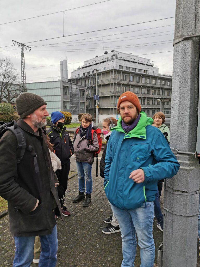 Gruppe von Personen steht an einer Straße vor einem großen Gebäude.