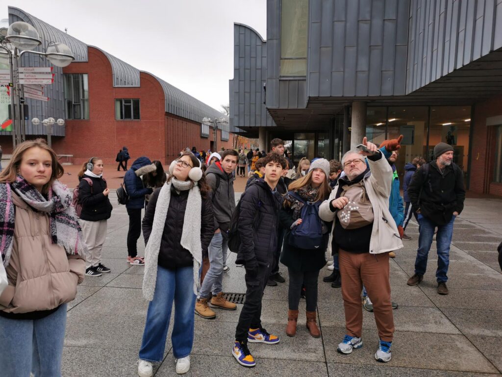 Grupp von Schülern stehend vor einem modernen Gebäude, einige schauen nach oben.