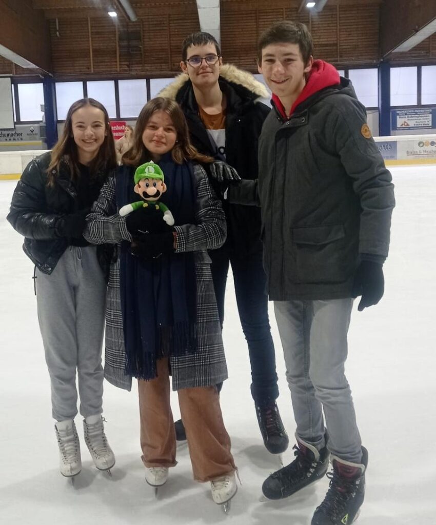 Gruppenfoto von vier Personen auf einer Eislauffläche, alle lächeln.