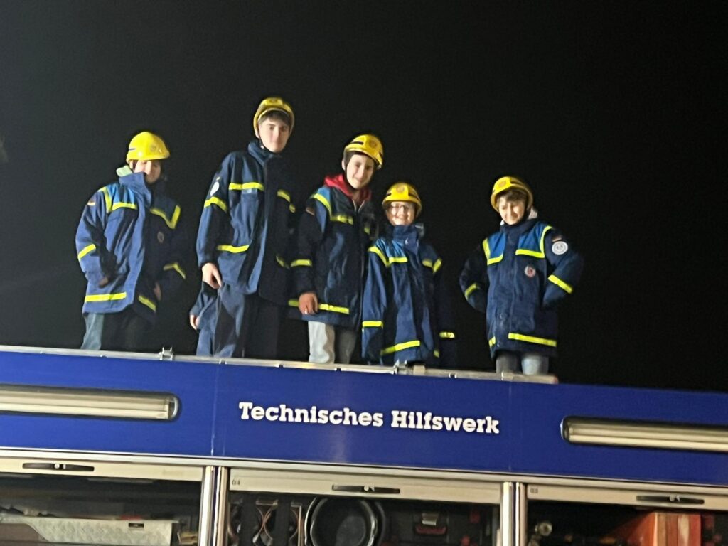 Kinder in Feuerwehrhelmen stehen auf einem Einsatzfahrzeug des Technischen Hilfswerks.