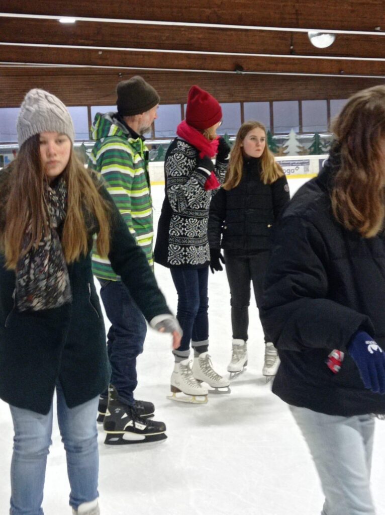 Eisläuferinnen und Eisläufer in einer Eishalle bei verschiedenen Aktivitäten.