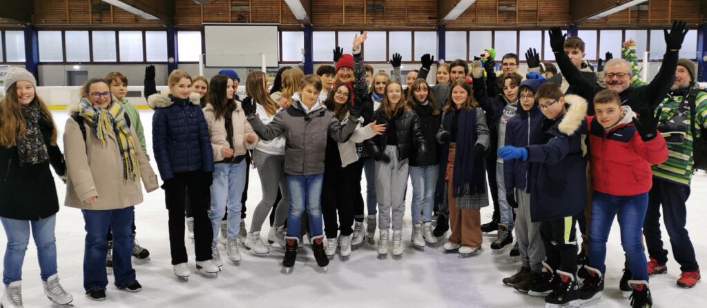 Gruppe von Jugendlichen und Erwachsenen auf einer Eisbahn, alle in Schlittschuhen.