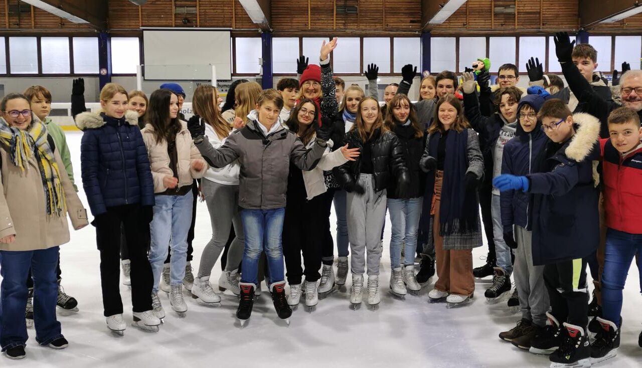 Gruppe von Jugendlichen und Erwachsenen auf einer Eisbahn, alle in Schlittschuhen.
