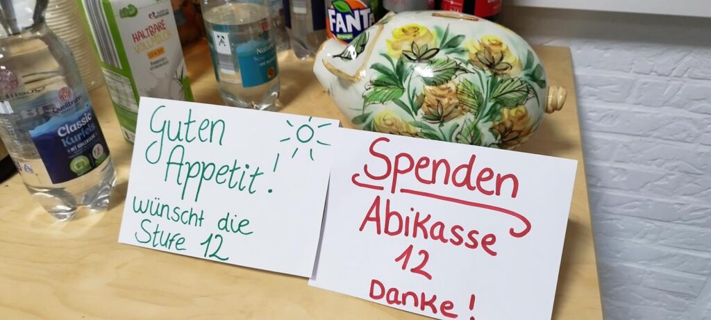 Tisch mit Wasserflaschen, Teekanne und zwei Schildern zu Spenden und Gutem Appetit.