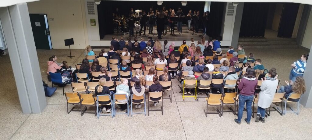 Schüler sitzen in Stuhlreihen und beobachten ein Konzert auf der Bühne.