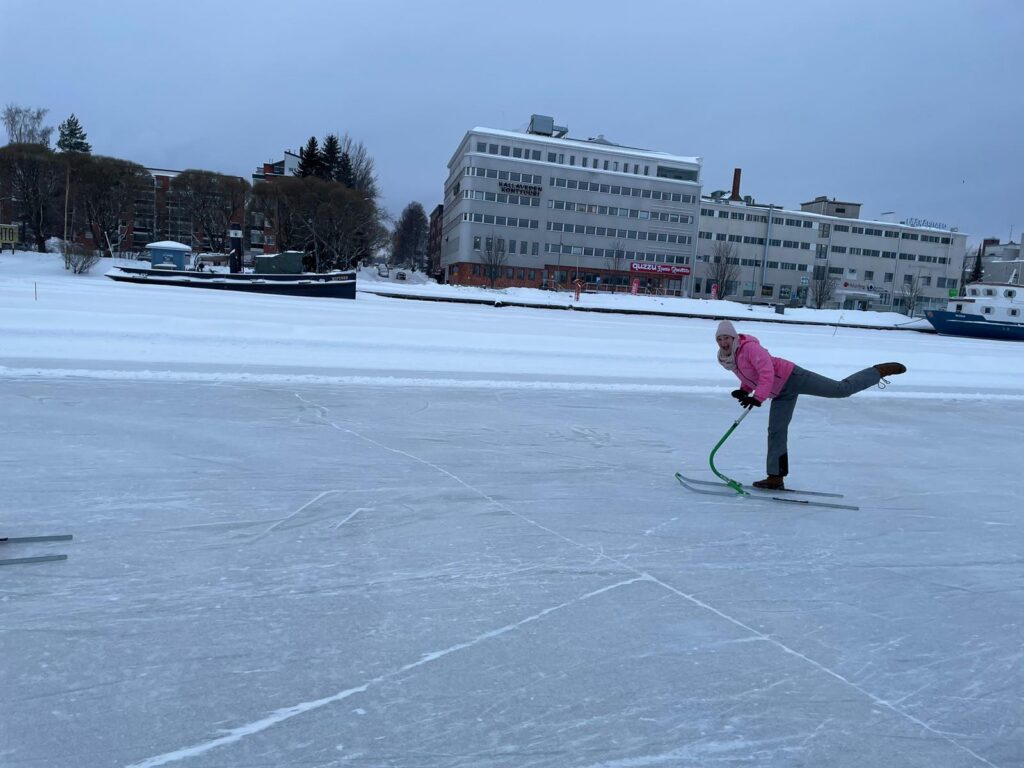 Person in pinkem Outfit macht Einzelbeinsprung auf einer gefrorenen Fläche.