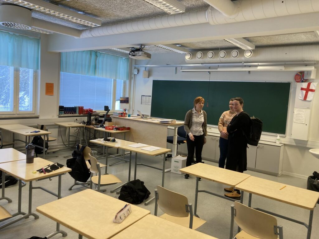 Drei Schüler stehen im Klassenraum zwischen leeren Tischen.