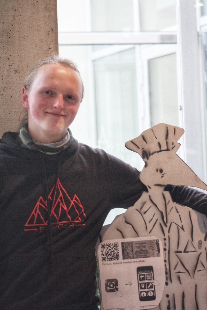 Junge mit Kapuzenpullover steht neben einer Pappfigur eines Kochs.