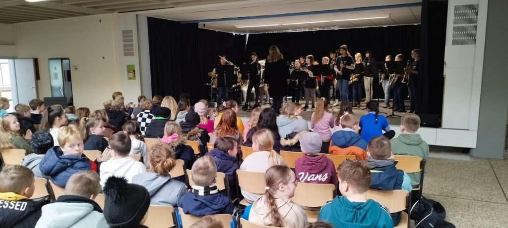 Schüler sitzen vor einer Bühne mit einer Band während einer Aufführung.