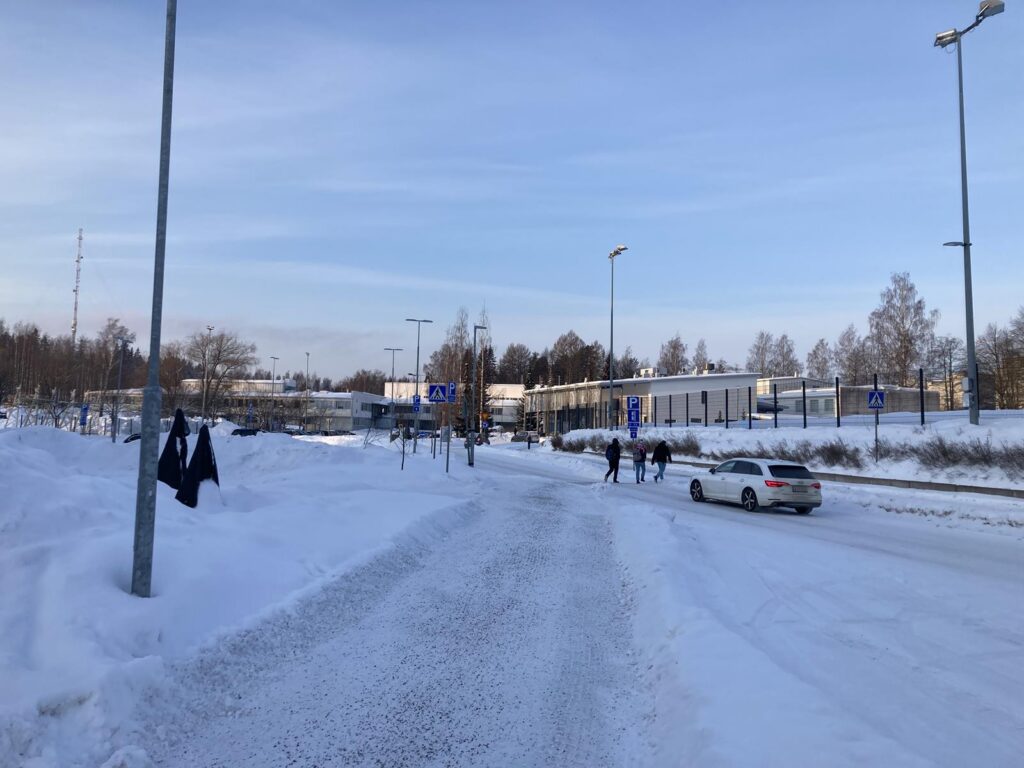 Schneebedeckte Straße mit Fußgängern und einem Auto. Im Hintergrund Gebäude.