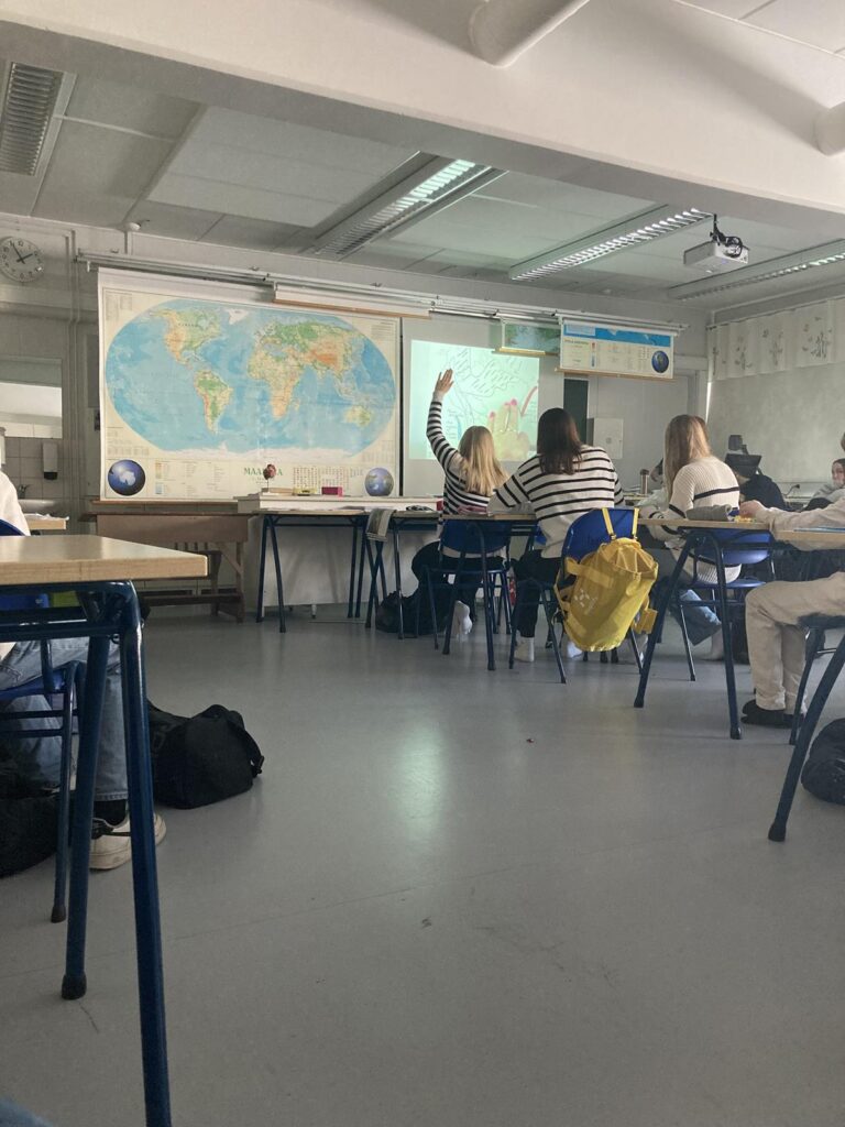 Schüler in einem Klassenzimmer mit Weltkarte und Präsentation.