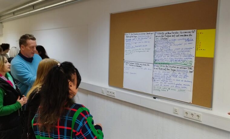 Gruppen von Personen stehen vor einer Wand mit Notizen und Skizzen.
