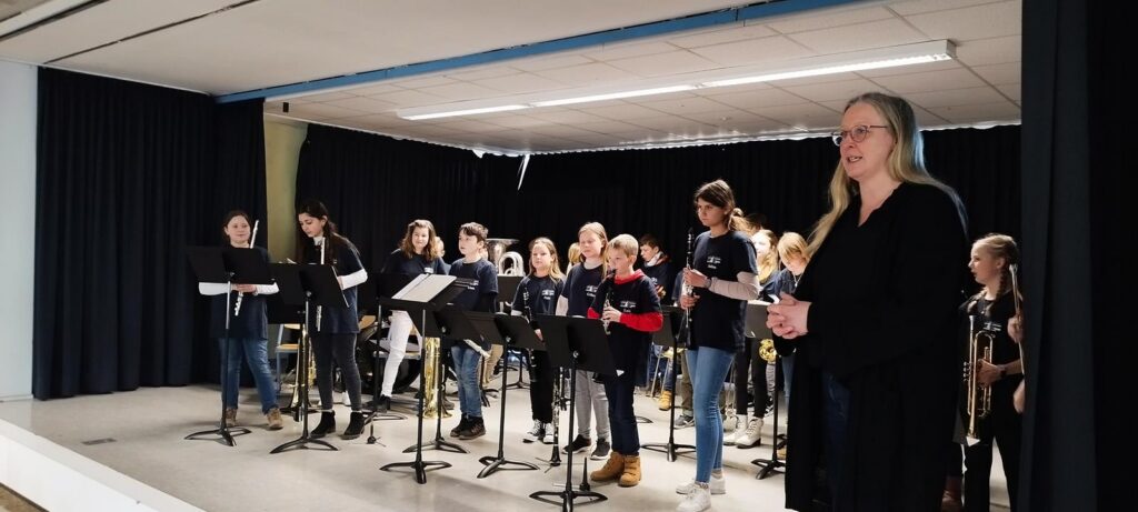 Schülerinnen und Schüler spielen in einer Aula Musik mit einer Lehrerin.
