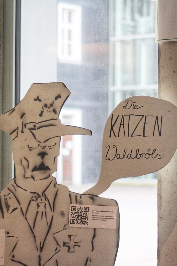Eine Pappfigur in Uniform mit Sprechblase über Katzen.