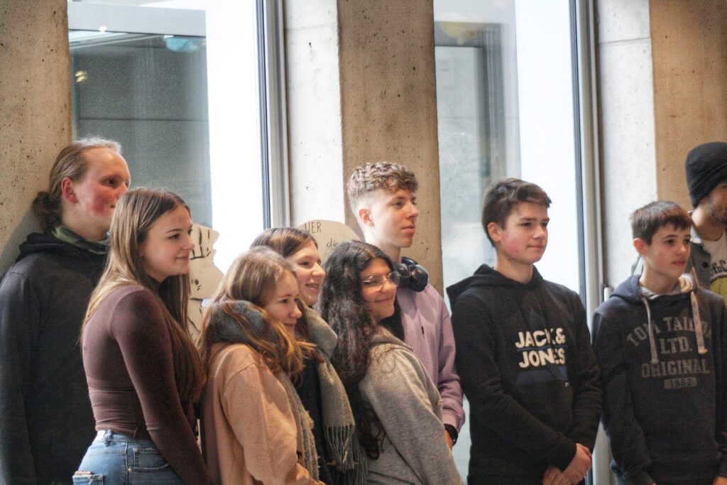Gruppe von Jugendlichen steht lächelnd vor Fenstern.