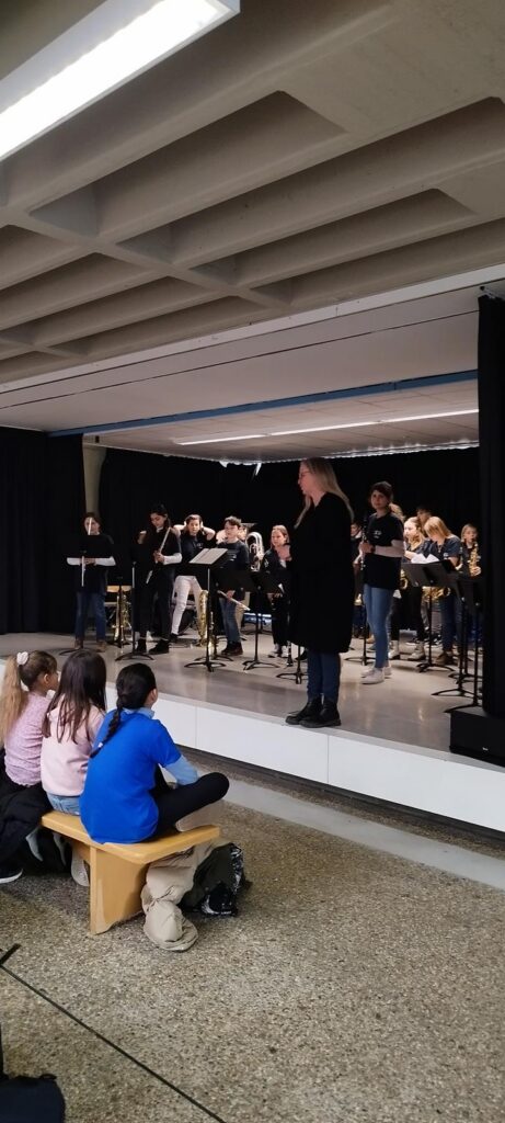 Schulband spielt auf einer Bühne, Zuschauer sitzen davor.