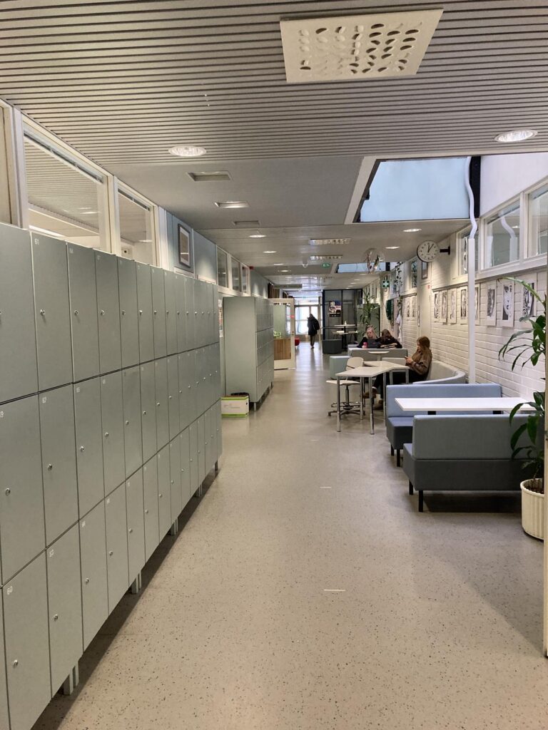 Ein Flur mit Spinden, Tischen und Stühlen in einer Schule.